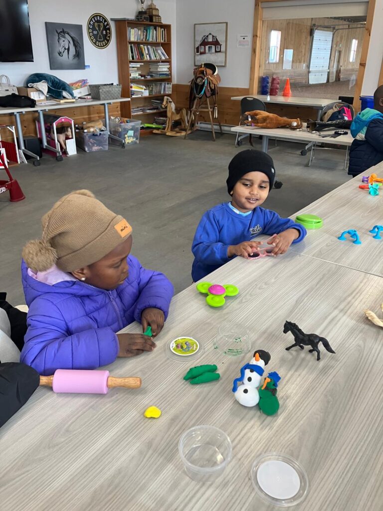 Two children playing with horse figurines and crafts at Rainbow Riders activity table
